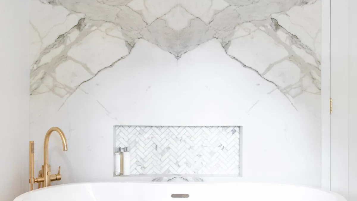 Book-matched marble-effect porcelain feature wall behind a freestanding bath