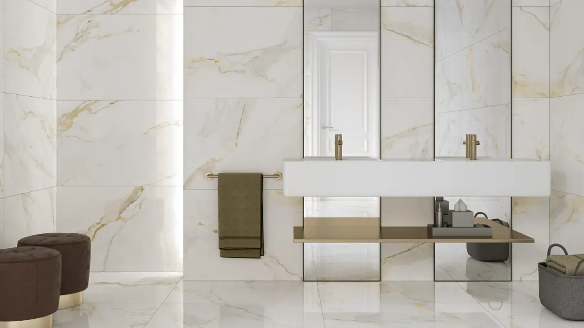 Wide-angle view of a luxury bathroom fully tiled in large-format Calacatta marble-effect porcelain, with a frameless glass walk-in shower, wall-hung basin, brushed brass brassware and near-invisible grout lines